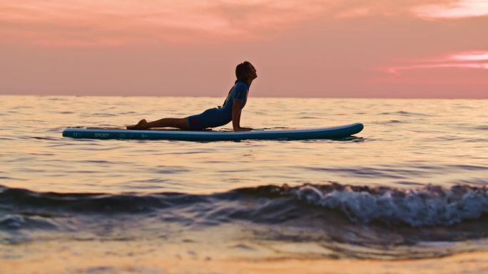 柔韧性的女子在日落时在田园诗般的海上桨板上练习瑜伽的慢镜头