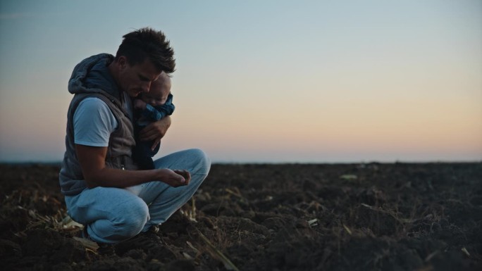 SLO MO男环保人士在日落时分带着儿子在农场播种前检查土壤质量