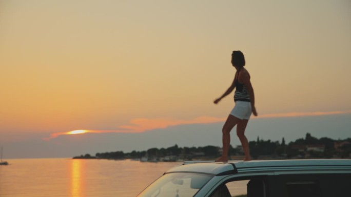 日落时分在海边露营车上悠闲跳舞的女子的慢镜头镜头