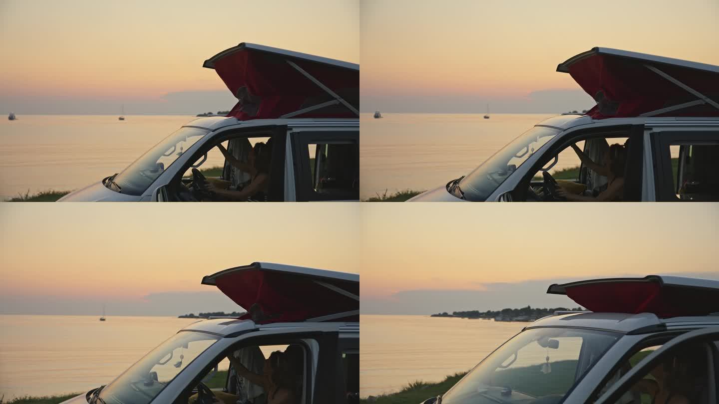 日落时分，女人坐在露营车里关闭海边屋顶上的帐篷