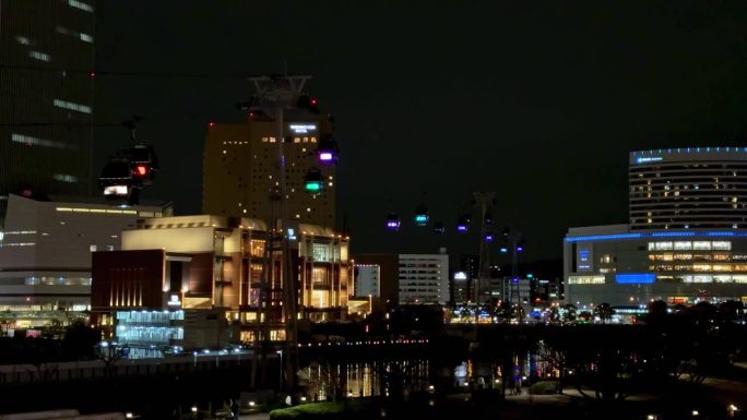 夜晚的城市天际线，明亮的灯光反射在水面上，建筑起重机点缀在背景中