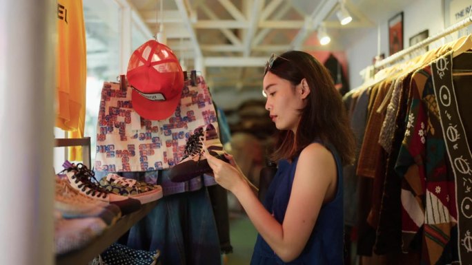 年轻的亚洲女游客背着背包在当地的街头市场购物。