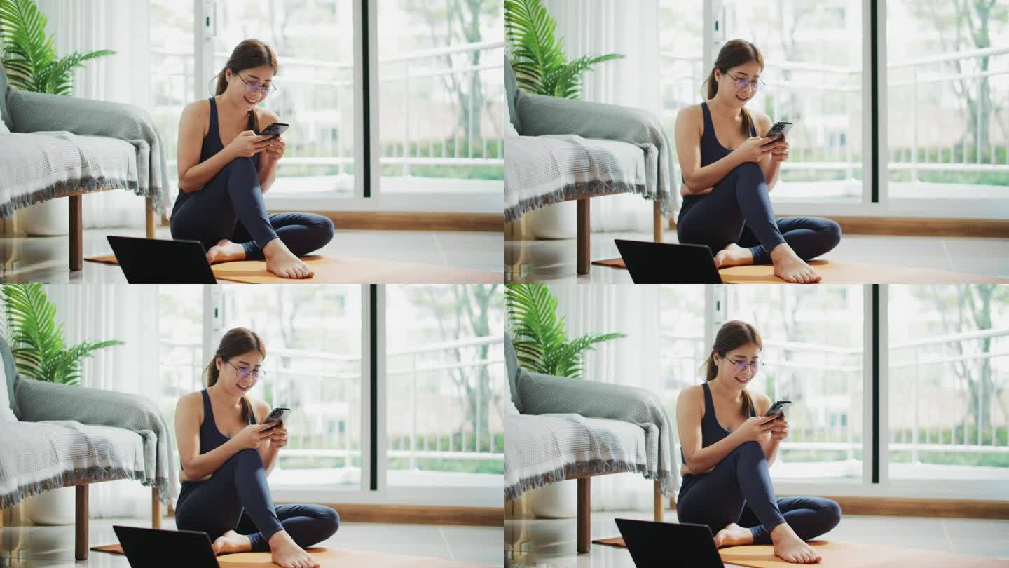 一名女子在家训练后坐在窗台上玩智能手机