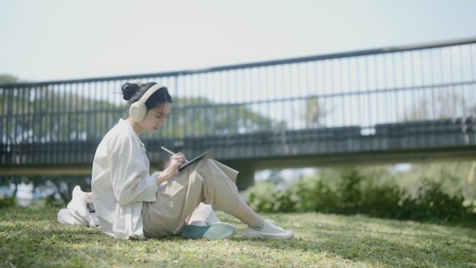 一个十几岁的女孩坐在公园的草地上，戴着耳机听着她最喜欢的歌。