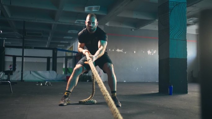 在体育馆里，强壮的男运动员正在用绳子拉重物