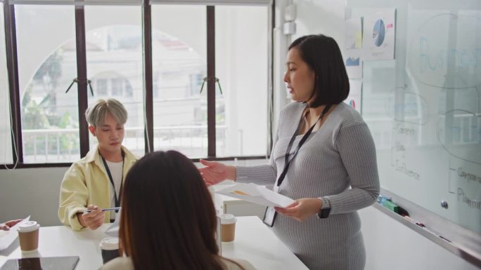 怀孕的女商人在现代办公室里与同事们围坐在桌子旁开报告会