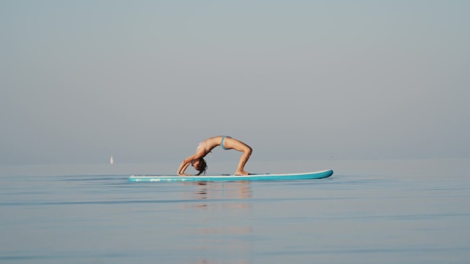 在阳光明媚的日子里，活跃的比基尼女性在冲浪板上练习瑜伽