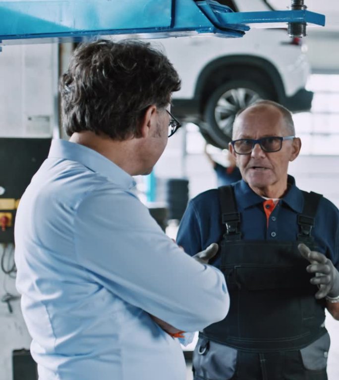 机械师和经理在汽车修理厂的汽车下谈话