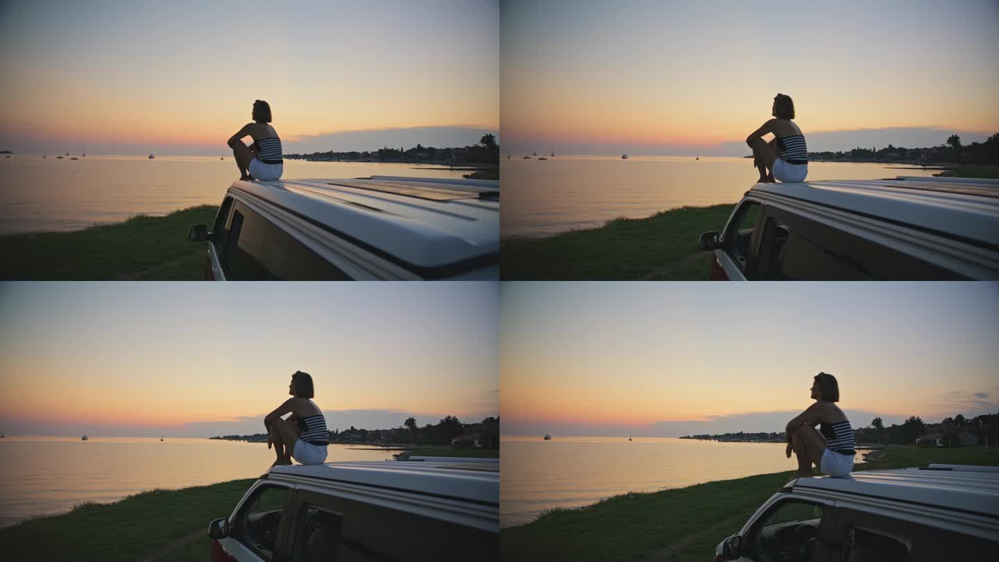 在周末度假期间，在面包车顶部观看宁静日落景色的女子的SLO MO镜头