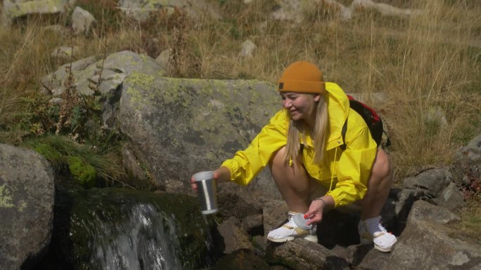 一位女性旅行者在夏季的森林里从河流或泉水中饮用干净的水。徒步旅行时，背着背包的女游客喝着新鲜的山水