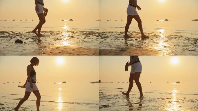 日落时分，女子手拿拖鞋走在沙滩上的慢镜头