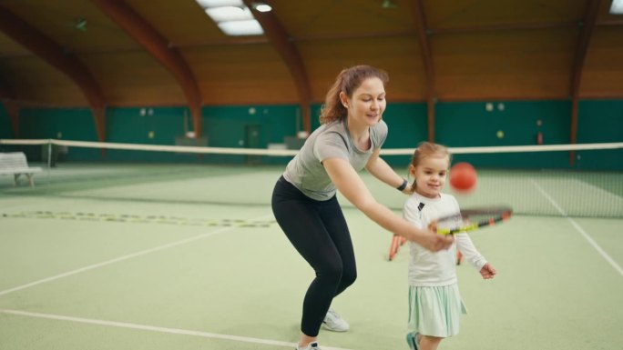 体育俱乐部训练中，年轻女教练协助女孩拍网球