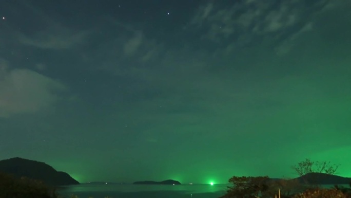 明亮的绿色星光在深蓝色的星空上，在平静的海洋海水中轮廓山林