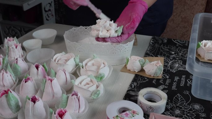 自由职业者在家做棉花糖。一位妇女把糖粉撒在棉花糖花上。用刷子去除多余的部分。棉花糖玫瑰和郁金香摆在桌