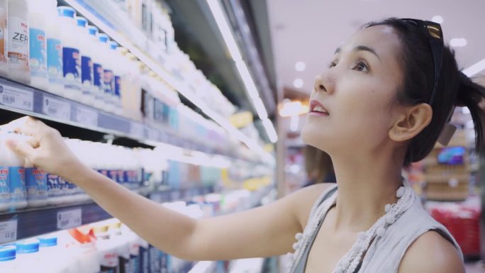 美丽的亚洲女人选择和购买牛奶在杂货店超市。