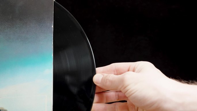 一名男子从蓝色套筒里拿出一张黑胶唱片，黑色背景的滑块。