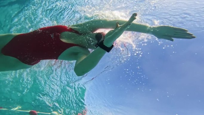 在阳光明媚的日子里，坚定的运动女子在泳池里练习爬泳的低角度水下镜头