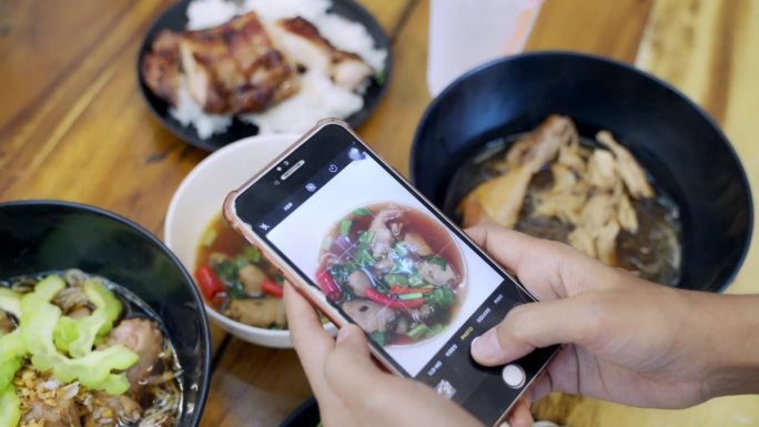 亚洲女性网红在泰国餐厅用智能手机拍摄食物。