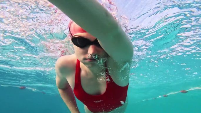 在阳光明媚的日子里，坚定的红色泳装女子在游泳池里练习自由泳的水下特写镜头