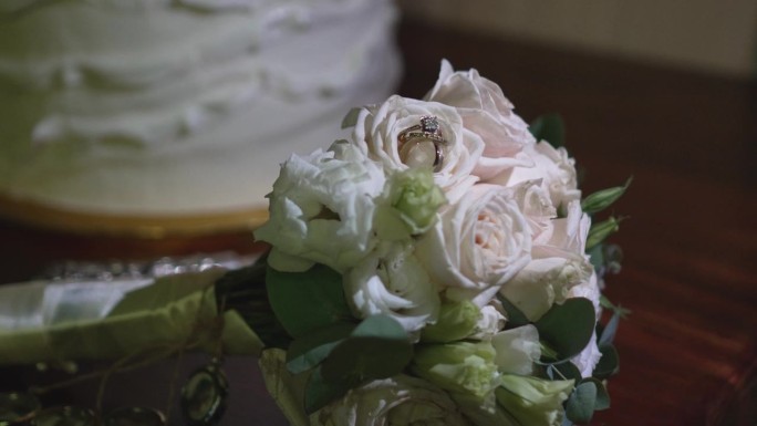 新娘捧花上闪闪发光的结婚戒指镶嵌在白玫瑰花瓣之间。婚礼的细节