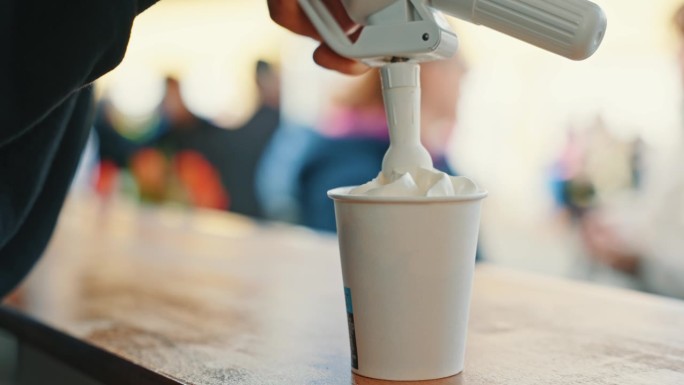 不明咖啡车老板将鲜奶油挤进纸杯的特写