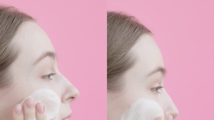 20多岁的金发女郎正在用粉色背景的洁面泡沫洗脸。