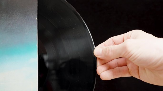 滑块镜头的特写，一个男人的手把黑胶唱片放进一个蓝色的袖子。孤立在一个黑色的背景。