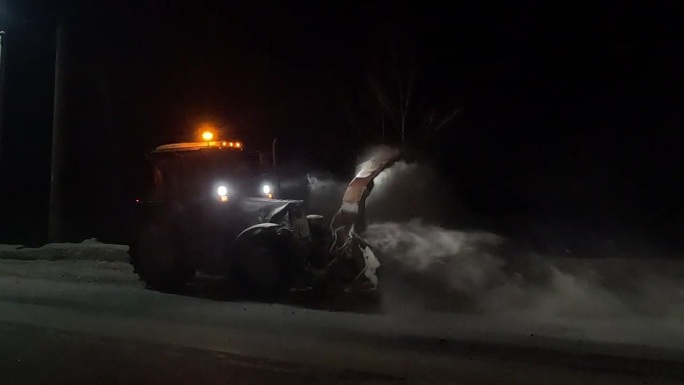 以拖拉机形式出现的除雪设备，在夜间作业，将道路上的雪扔进沟里
