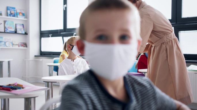 教师和儿童在教室室内戴口罩，消毒课桌。