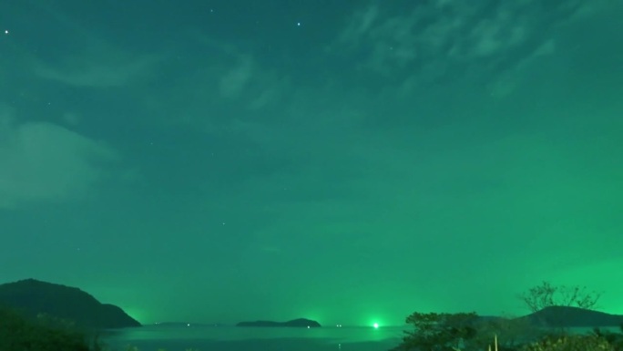 泰国普吉岛，夜晚的星空和绿色的星光在平静的海浪和海水中与渔船在一起