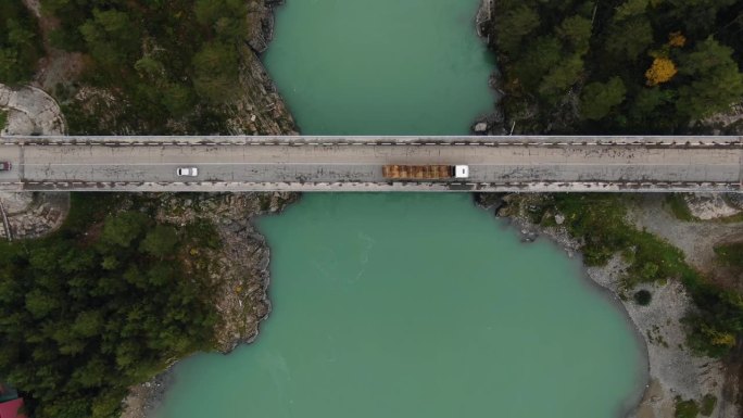 无人机直接捕捉到车辆在绿松石河上过桥的画面，河的两边都是树木