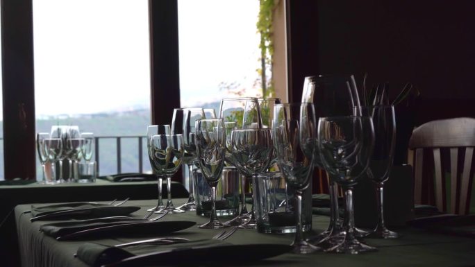 豪华餐厅里优雅的餐桌布置，窗外的自然风光尽收眼底，水晶高脚杯、墨绿色餐巾纸和餐具为客人准备。美丽的宴