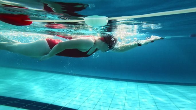在阳光明媚的日子里，坚定的运动女子在游泳池游泳的水下跟踪镜头