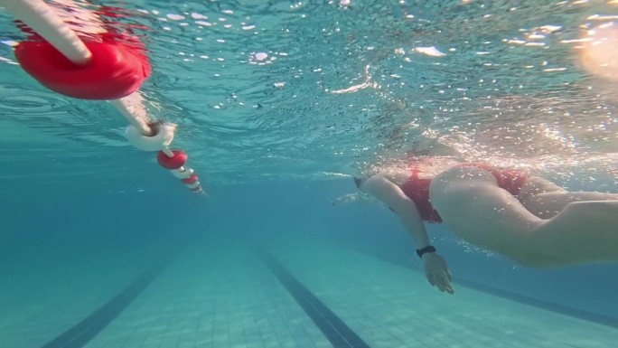 在阳光明媚的日子里，穿着红色潜水服的运动年轻女子在游泳池游泳的水下侧视图跟踪拍摄