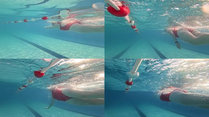 在阳光明媚的日子里，穿着红色潜水服的运动年轻女子在游泳池游泳的水下侧视图跟踪拍摄