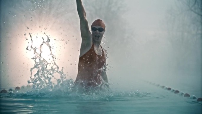 在度假胜地雾蒙蒙的早晨，兴奋的运动女性从游泳池里出来，举起手臂尖叫