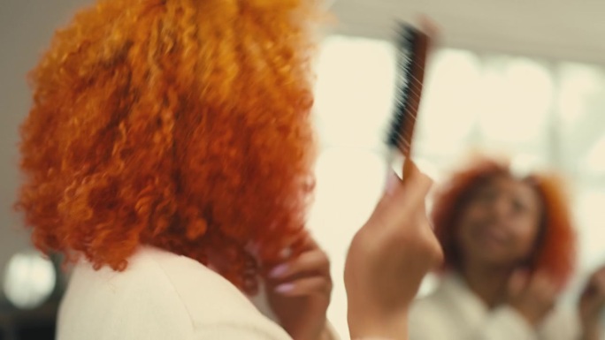 年轻女子在镜子前梳理红色卷发，增加头发的蓬松度