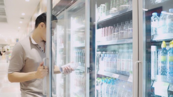一名亚洲男子从超市的冷冻箱中取出瓶装水。