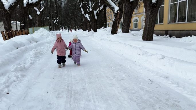 城市公园里，两个小妹妹用绳子拉着坐在雪橇上的第三个妹妹