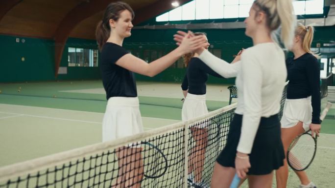 在体育俱乐部的球场上，快乐的年轻女子网球选手在比赛结束后与对手在网前握手