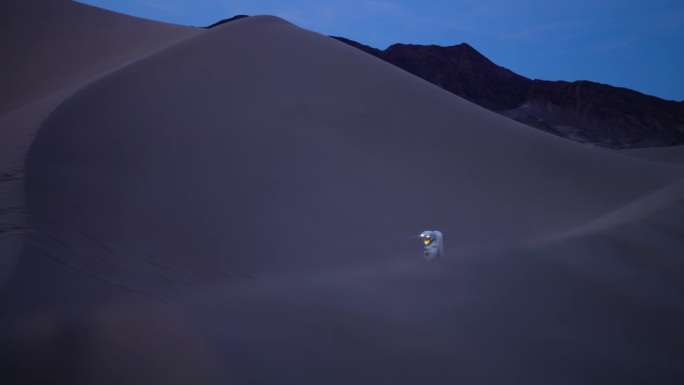 宇航员在沙丘上行走，穿着带灯的太空服，昏暗的夜晚