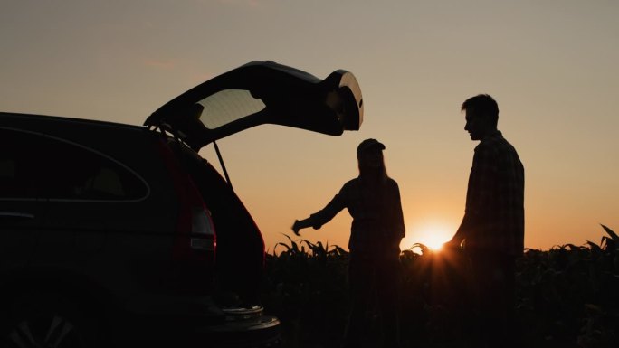 一对年轻夫妇在一辆破汽车前争吵。汽车停在玉米田的一边