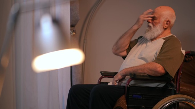 一个孤独的大胡子老人坐着，开着轮椅来到一扇拉着窗帘的窗前。一个残疾人从拉着窗帘的窗户往外看，用手摸了