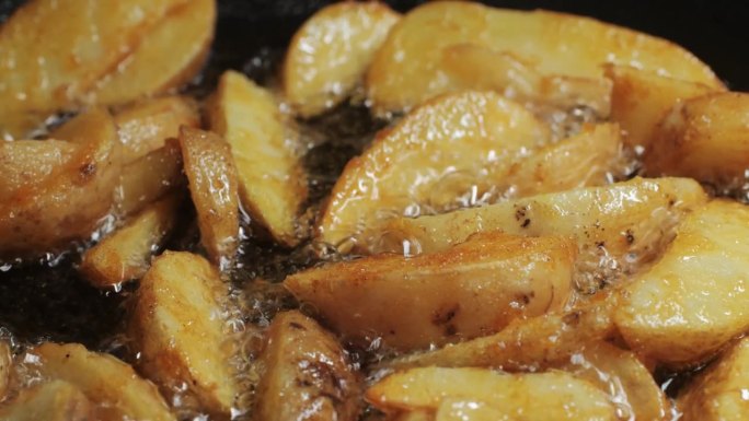 制作煎土豆角，乡村土豆在锅里沸腾的油特写。土豆片是休闲食品。厨师在咖啡厅厨房做饭。