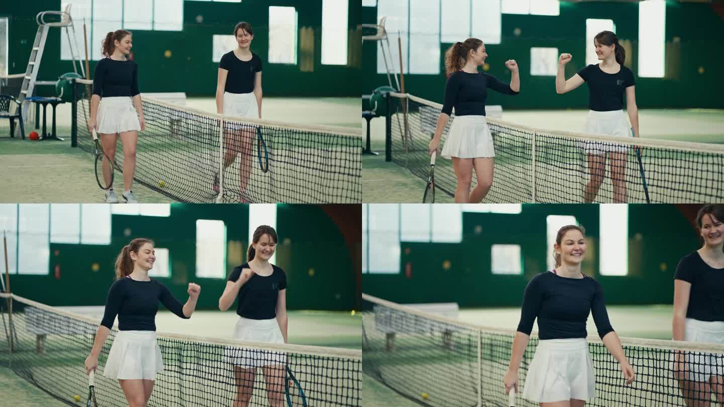 体育俱乐部的女网球选手们在比赛结束后微笑着互相碰拳，沿着网走