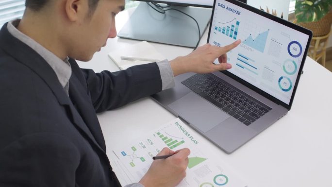 亚洲商人在笔记本电脑上分析财务数据，预测商业营销在现代办公室的发展趋势
