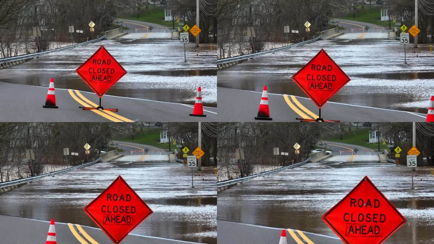 前方道路封闭标志，背景是被水淹没的街道和桥梁。美国自然灾害航拍图。