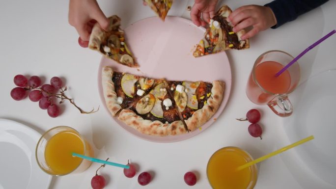 三对孩子的手从一个粉红色的盘子里拿出一块块巧克力披萨。
