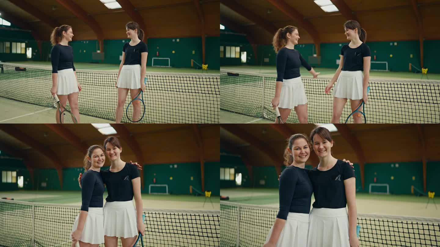在体育俱乐部的球场上，年轻的女网球运动员抱着球拍，手挽着手，望着镜头微笑的肖像