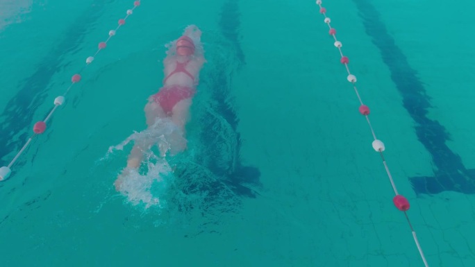 SLO MO高角度跟踪后景拍摄运动的年轻女子在游泳池游泳的红色泳衣